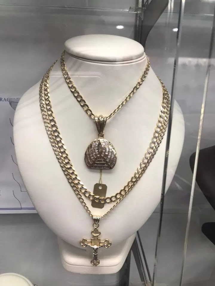 Layered yellow gold Cuban link chains with a baguette diamond dome pendant and a gold crucifix on a white display bust
