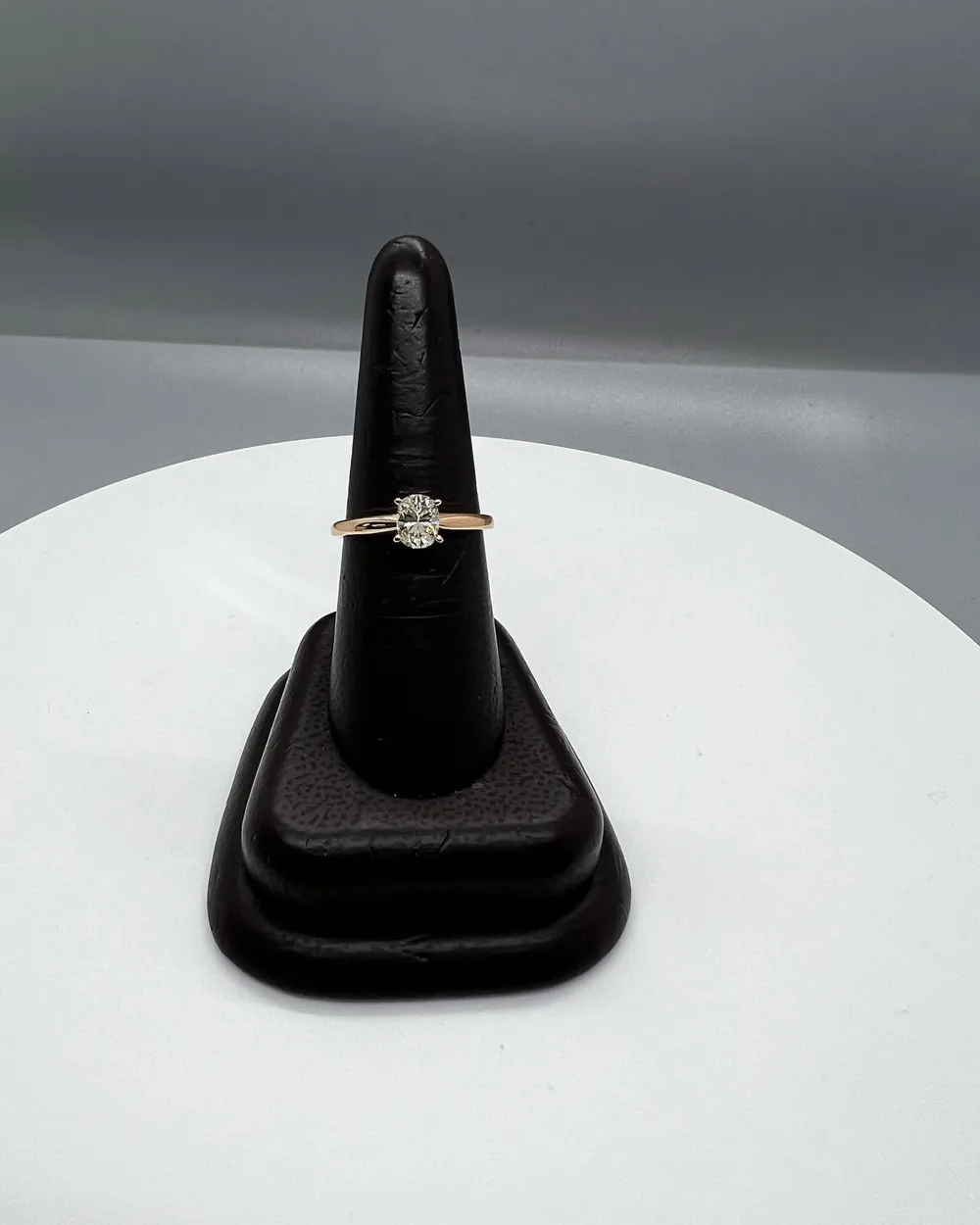 Oval diamond solitaire engagement ring with a rose gold band on a dark ring stand