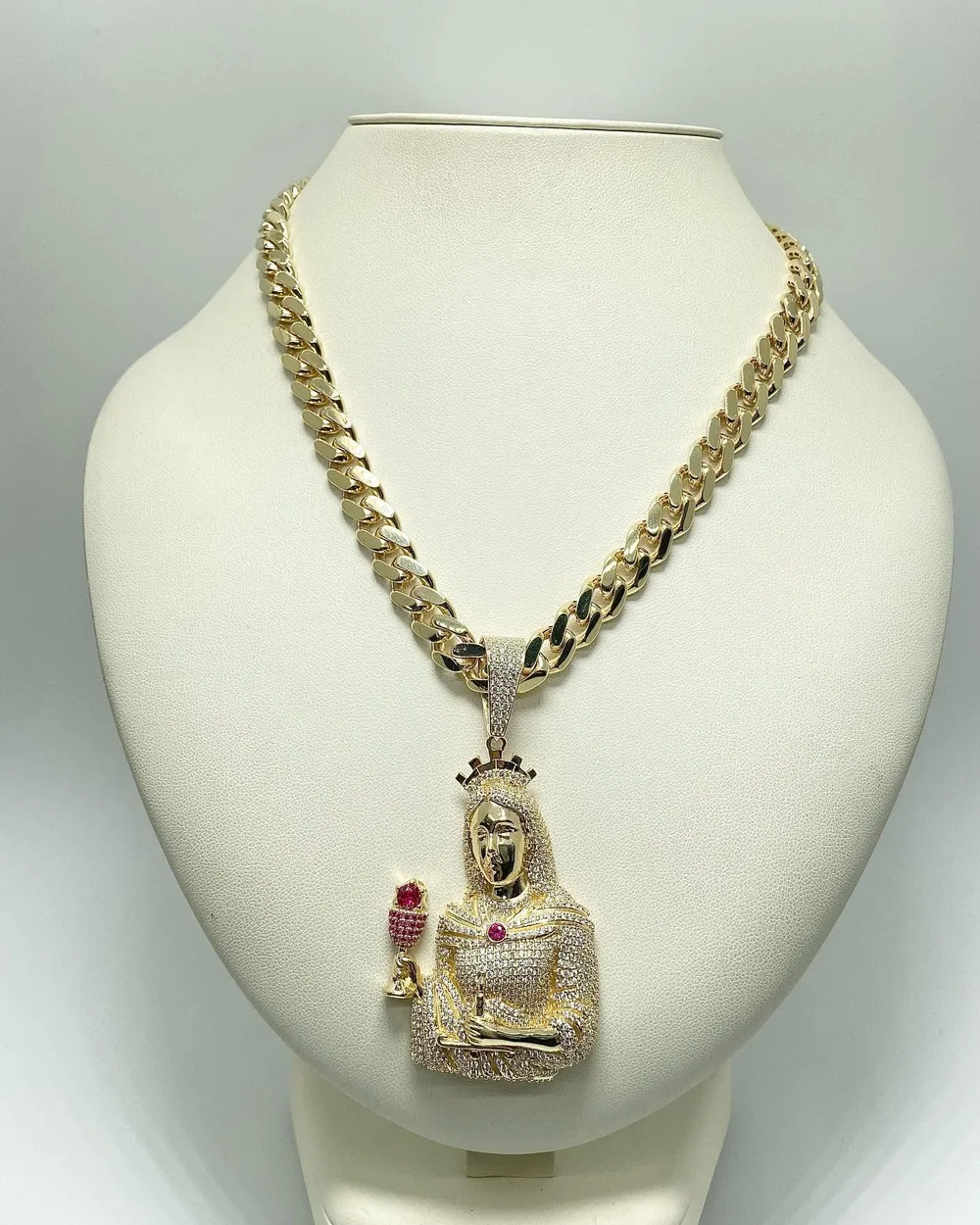 Pavé-set gold saint pendant with ruby accents on a yellow gold Cuban link chain, displayed on a white bust