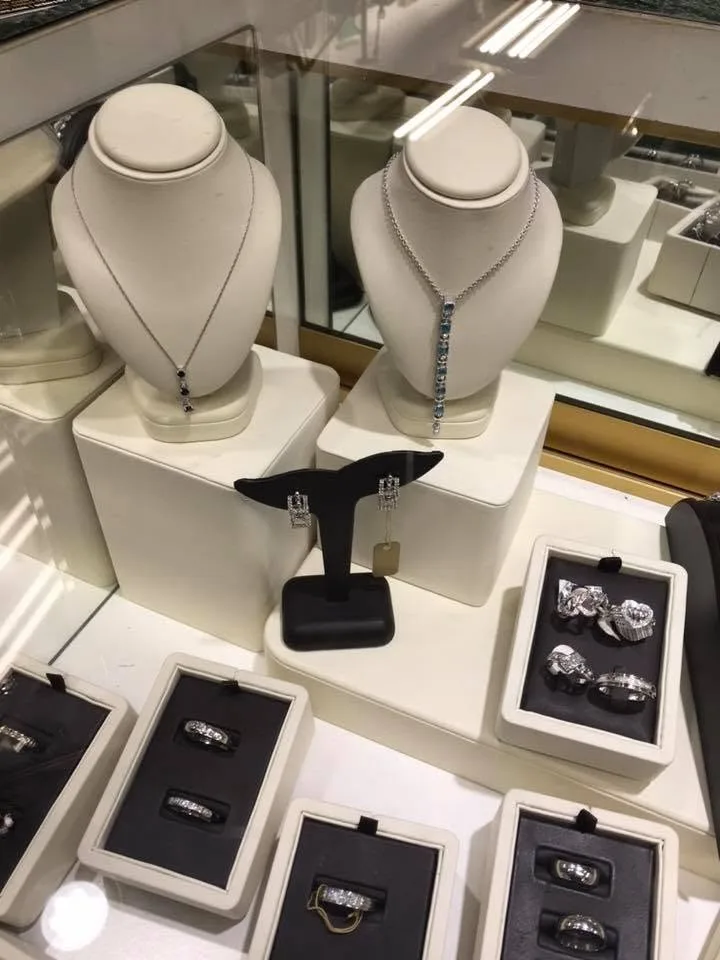 Diamond necklaces on white busts with earrings and wedding bands in the Capital Jewelry showroom case