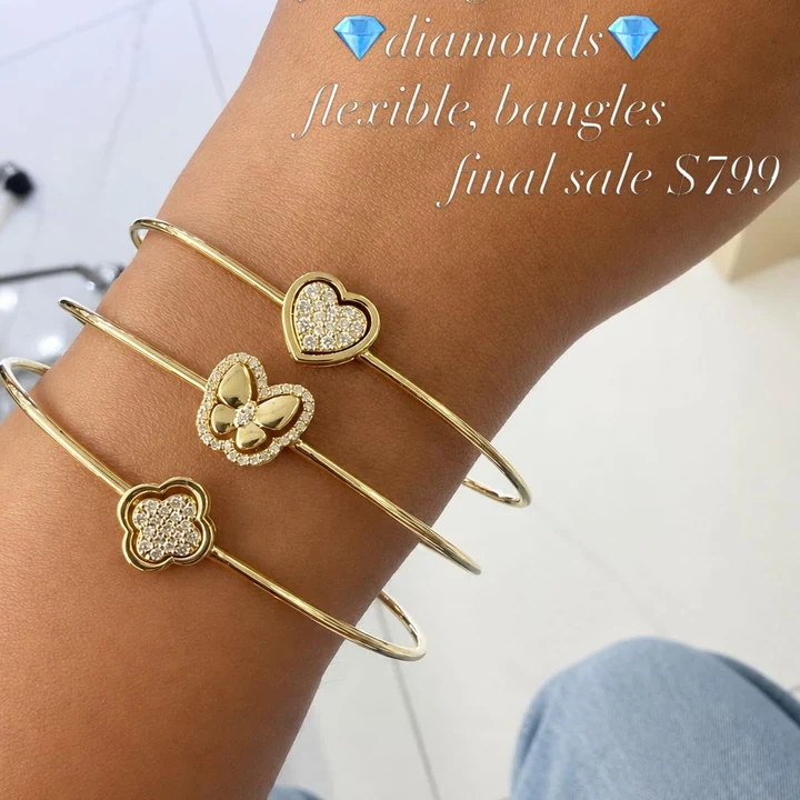 Three gold flexible bangles with diamond heart, butterfly and clover charms on the wrist