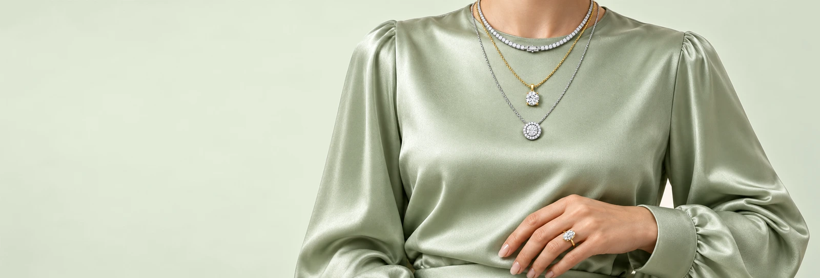 Woman in a sage satin blouse wearing a diamond tennis necklace layered with a solitaire pendant and a halo pendant, and a marquise diamond ring