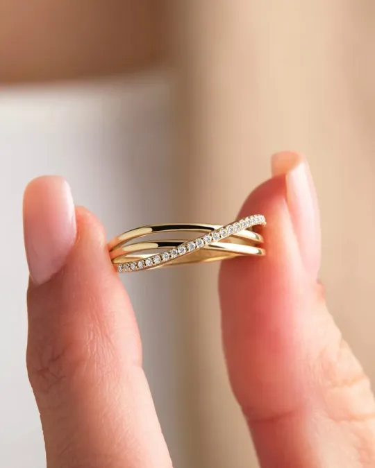 Yellow gold crossover ring with a pavé diamond band held between two fingers